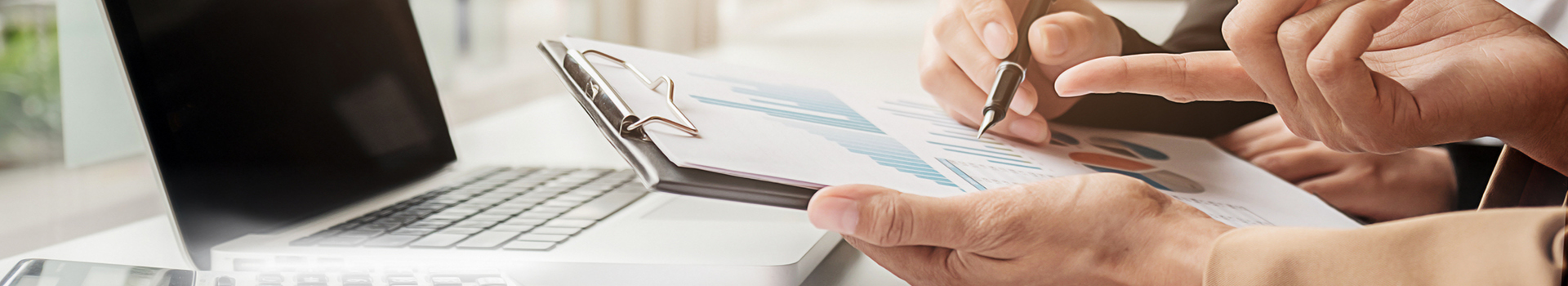 a close up of a person's hands holding a clipboard with a chart and sitting in front of a laptop